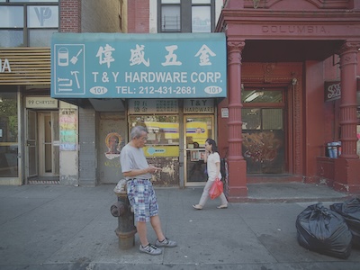 A man lens on a fire hydrant in front of a store in China Town. A woman walks behind him.