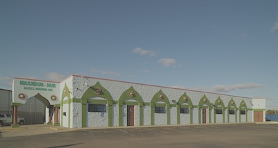 One-story white building with a “Masjidun-Nur” sign and green minaret designs.