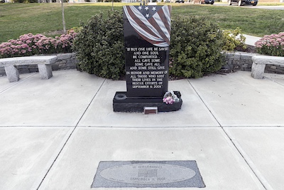 Black stone memorial resembling a large headstone that reads &ldquo;If but one life be saved and one soul be comforted&mldr; all gave some some gave all and some still give. In honor and memory of all those who lost their lives in the rescue efforts of September, 11, 2001.&rdquo; The stone is painted to look like an American flag is draped over the top.
