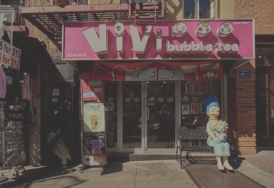 Store front reading Vivi Bubble Tea with a pink background. A statue of Marge Simpson sits on a bench in front of the store.