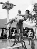 Photo, "A man standing on a ladder holds a swimsuit-clad woman over a pool of water, ready to toss her in," Cuyahoga County Fair, 1964 Photo, A man standing on a ladder holds a..., Cuyahoga County Fair, 1964